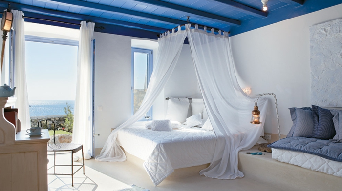 bleu grec sur le plafond en bois, lanterne à bougies, rideaux longs, lit à baldaquin