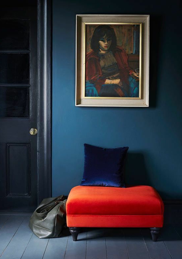 mur bleu canard, portrait de femme, tabouret rouge et coussin bleu 