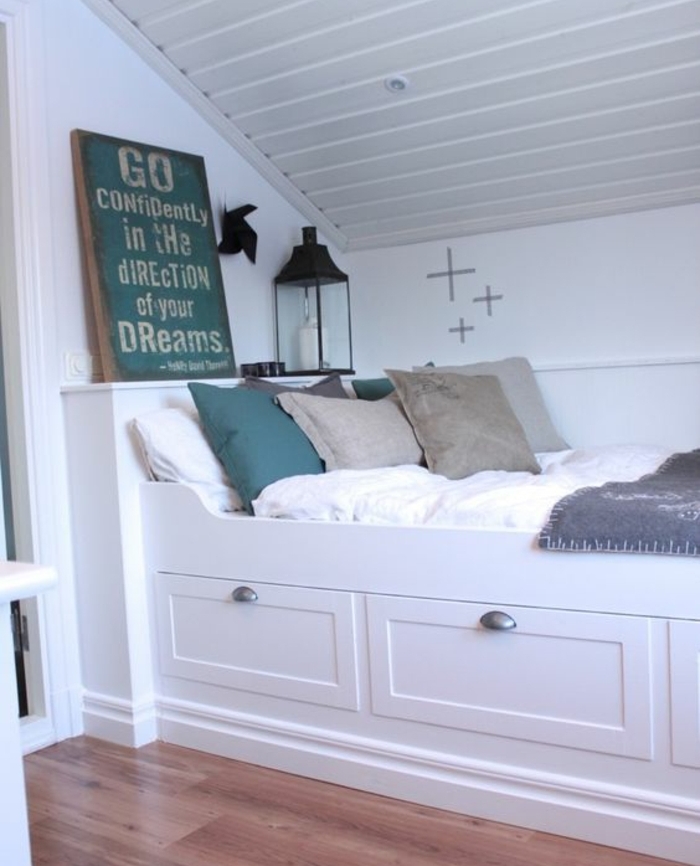 chambre sous combles minuscule, lit blanc avec rangements, linge de lit blanc, coussins gris et vert, parquet clair, peinture mur blanc, chhambre mansardée
