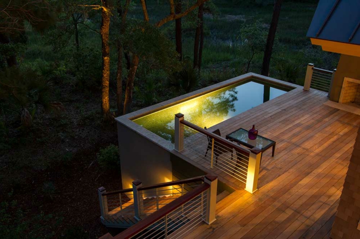 piscine hors sol rectangulaire, terrasse de piscine en bois, éclairage de piscine jaune, table basse, vue sur la forêt