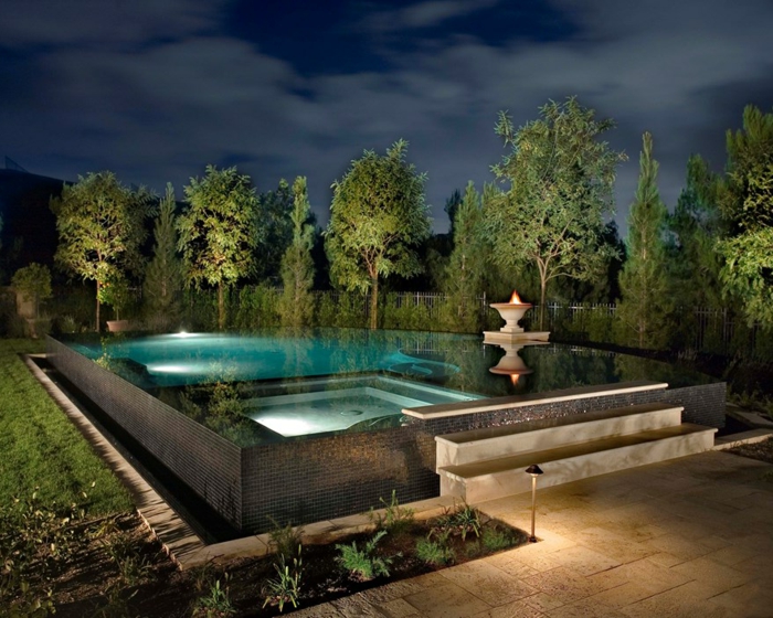 piscine hors sol rectangulaire, éclairage de nuit, fontaine avec feu, arbres verts