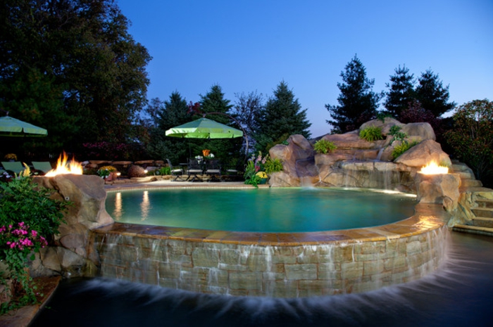 piscine hors sol en pierre, feu dans le jardin, parasols verts, cascades d'eau