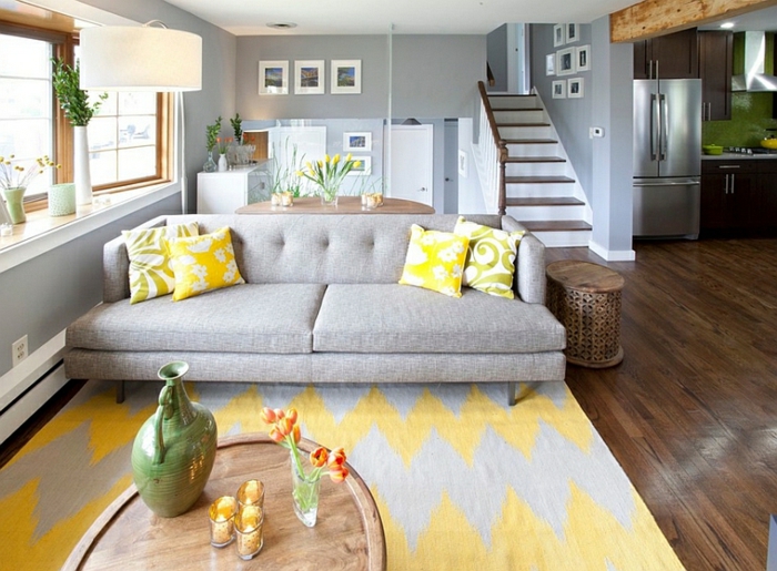 salon gris et jaune, tapis gris et table ovale en bois, coussins jaunes sur un grand sofa gris 