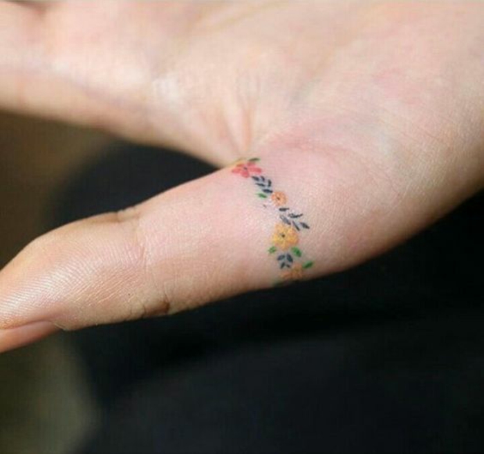 un tatouage sur le doigt dans l'esprit minimaliste, tatouage couronne de fleure coloré