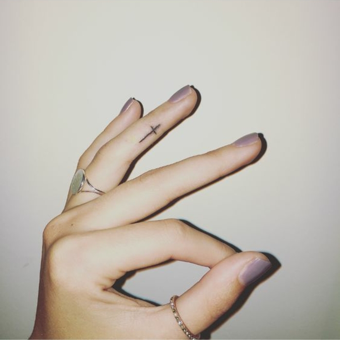 un tatouage main presque imperceptible, petite croix tatouée sur le côté du doigt