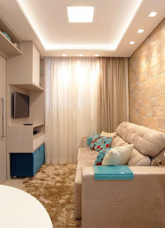 aménager une petite chambre, parement mural en pierre, tapis beige, grand sofa moelleux et tv suspendu