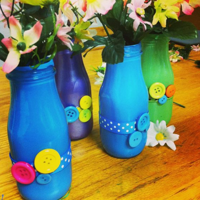 bouteilles en verre repeintes de couleurs diverses et customisés avec des boutons multicolores, vase de fleurs avec des bouquets de fleurs, cadeau pour la fête des mères