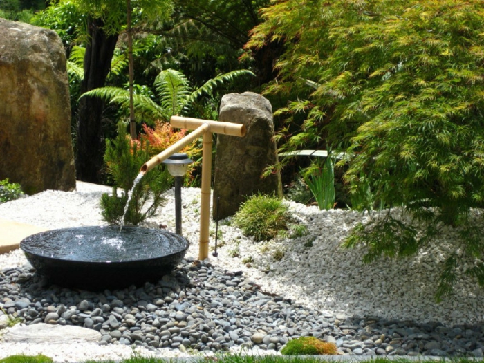 parterre de fleurs avec galets, fontaine zen en bambou, arbres verts, rochers dans le jardin
