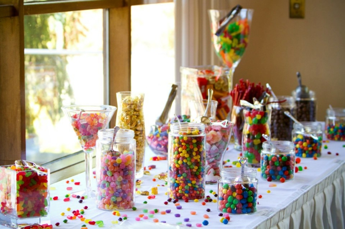 decoration bar a bonbon mutlicolore, dragées et boules de gomme rangée dans des récipients en verre, bocaux et verres, bonbons dispersés sur la table