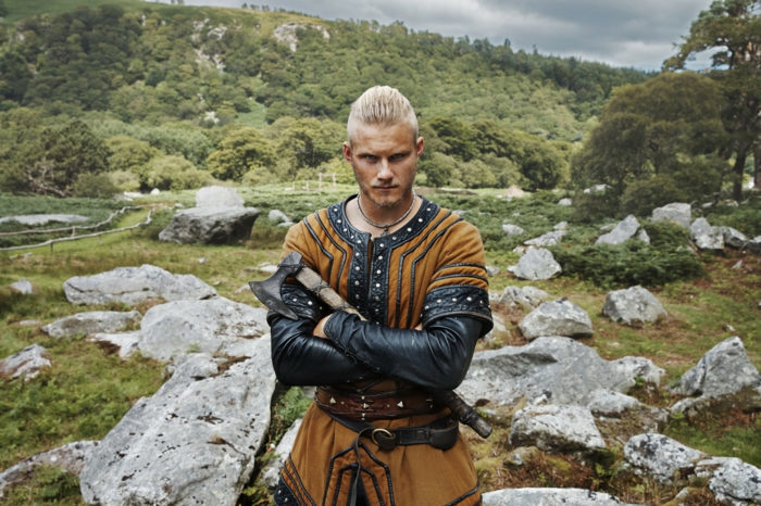 coupe de cheveux viking, bjorn lorthbrok, man bun, collier ethnique, chemise marron en cuir noir
