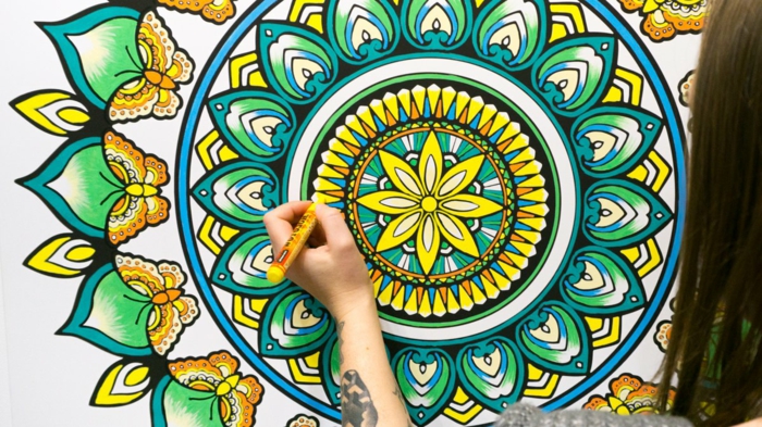 mandala à colorier, fleur jaune, feuilles vertes, volutes, papillons jaune et orange, filles, tatouage sur main