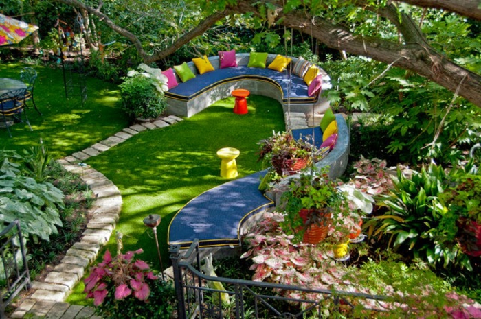 recup jardin, clôture en fer forgé, sentier en pierres, banc en tissu bleu, parasol multicolore, salon de jardin, table en verre