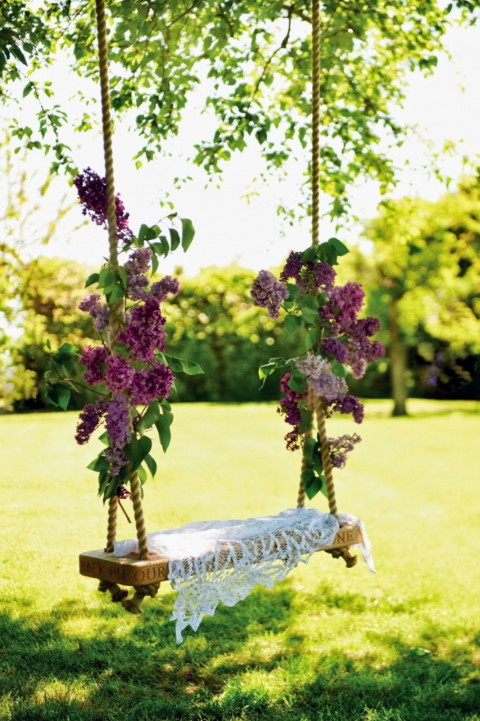 decoration exterieur de jardin, balançoire en bois, corde décorés en lilas, arbres, gazon vert