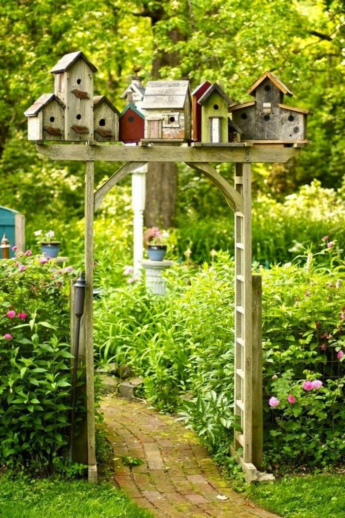 amenagement jardin, porte en bois, étagère avec mangeoires d'oiseaux, plantes vertes, sentier en pierre
