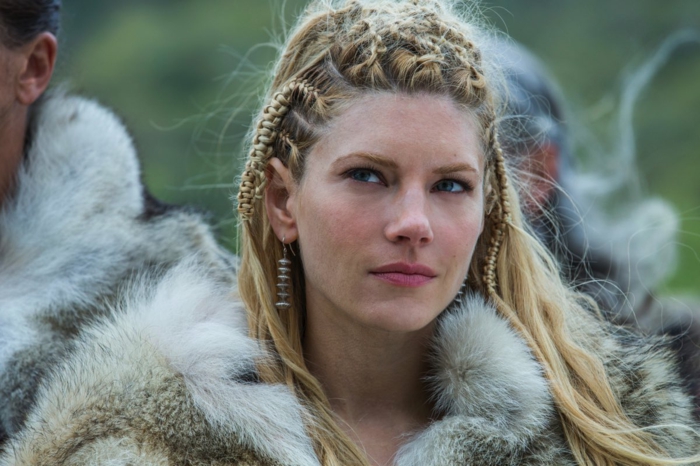 vikings lagertha, lèvres rose, manteau en simili fur, cheveux blonds tressés, boucles d'oreille en métal argenté