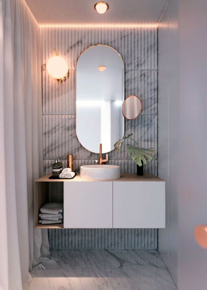 miroir lumineux salle de bain en forme ovale avec un petit miroir rond supplémentaire et un meuble suspendu