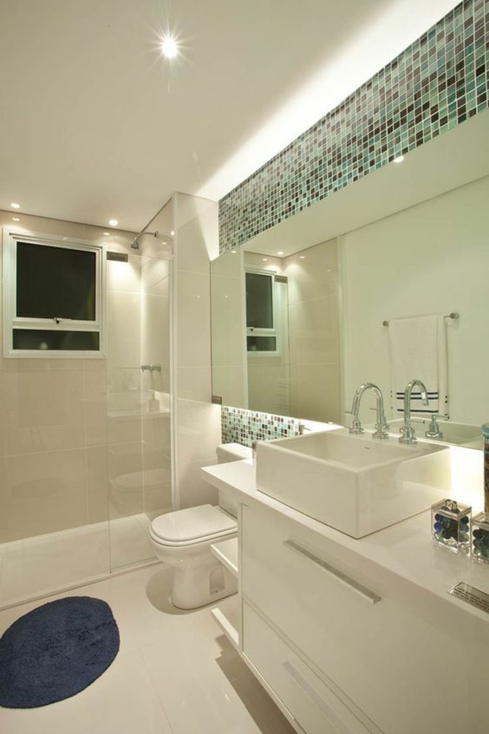 miroir lumineux de salle de bain avec des mosaiques en vert et gris foncé comme accents au-dessus et au-dessous du miroir