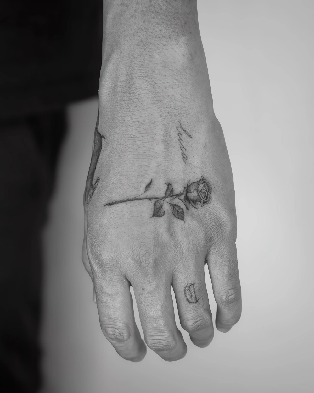 photo blanc et noir tatouage rose sur main doigts homme
