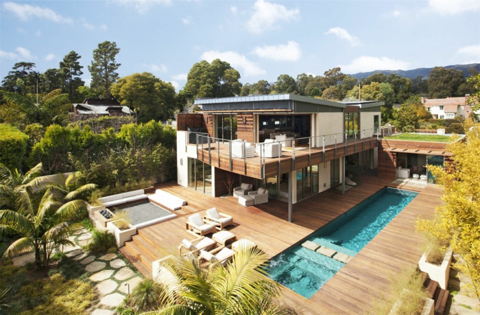 terrasse surélevée, façade en bois, piscine rectangulaire, transats blancs, salon de jardin blanc, arbres