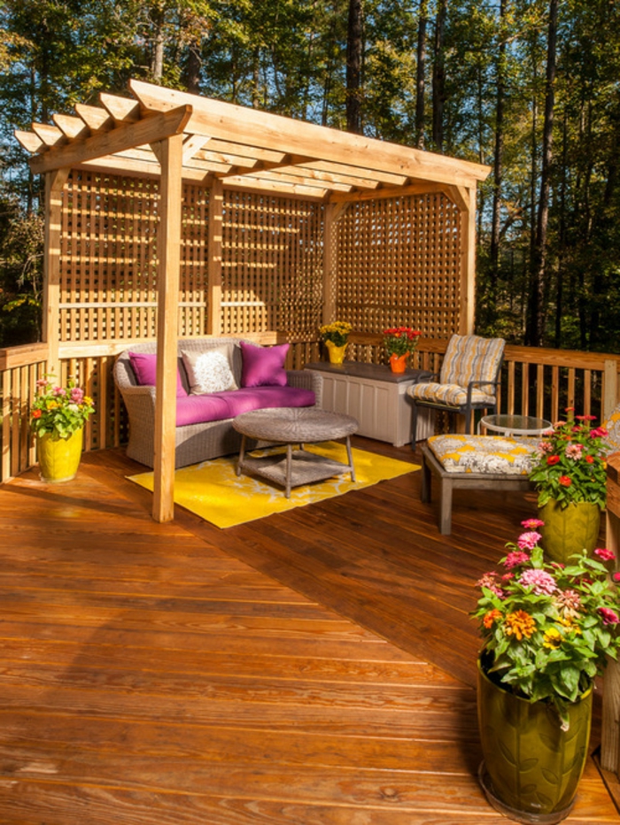terrasse surélevée, tapis jaune, table basse ronde, pot à fleur jaune, coussins rose, auvent en bois