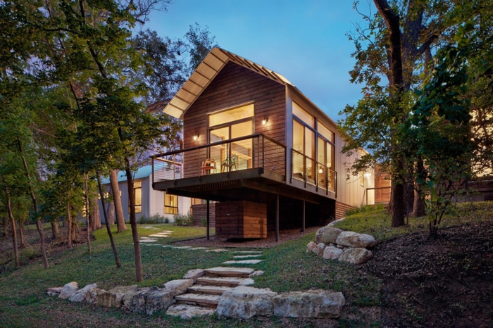 terrasse surélevée, maison en bois, grandes fenêtres, sentier en pierre, arbres, gazon vert