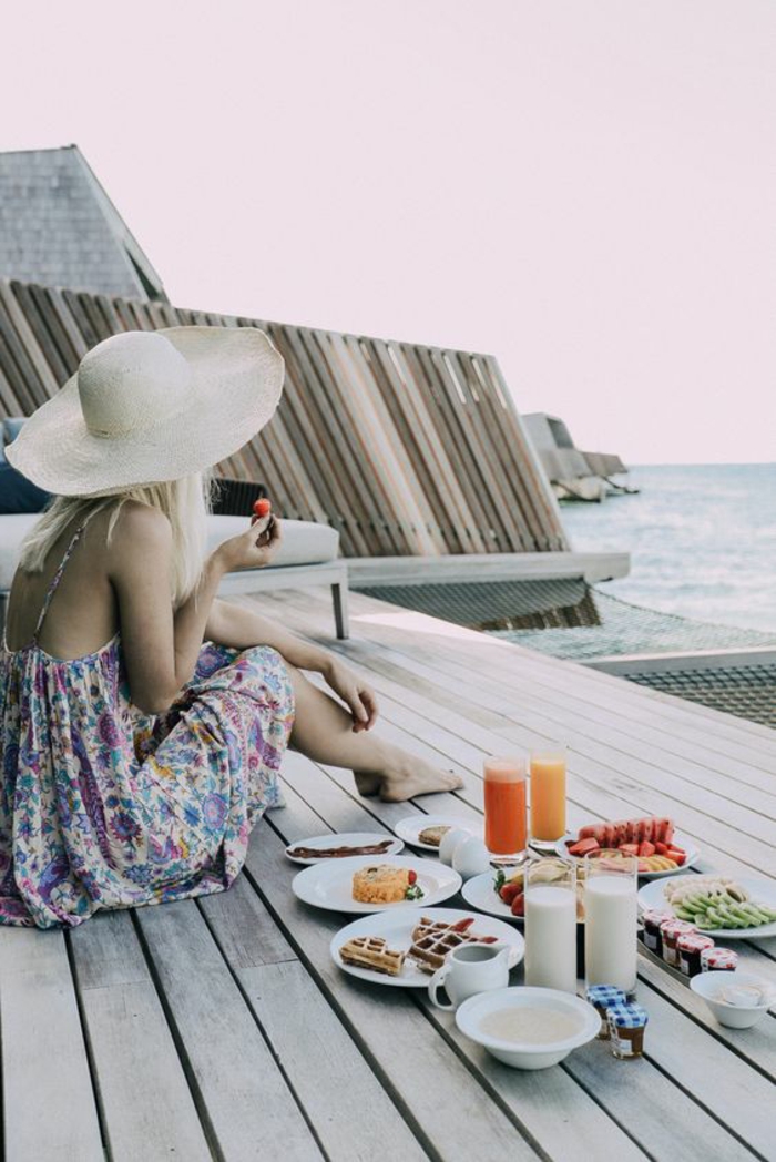 Déjeuner au bord de la mer - belle photo de femme qui mange son petit déjeuner habillée en robe imprimée fleurie bohème chic