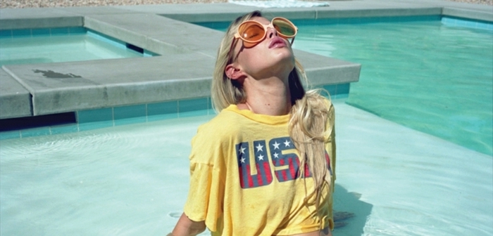 couleur blonde, t-shirt jaune avec lettres USA, rouge à lèvres rose, lunettes de soleil, cheveux longs raids