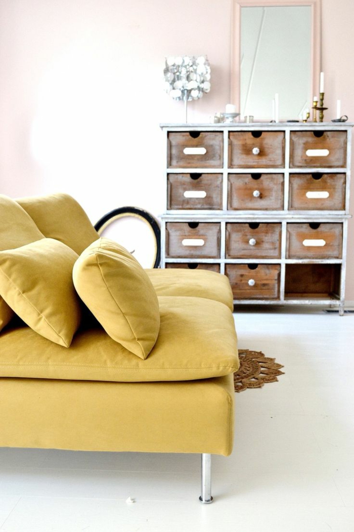 un canapé ocre jaune au design contemporain qui s'associe à un mur rose pastel et à un plancher blanc
