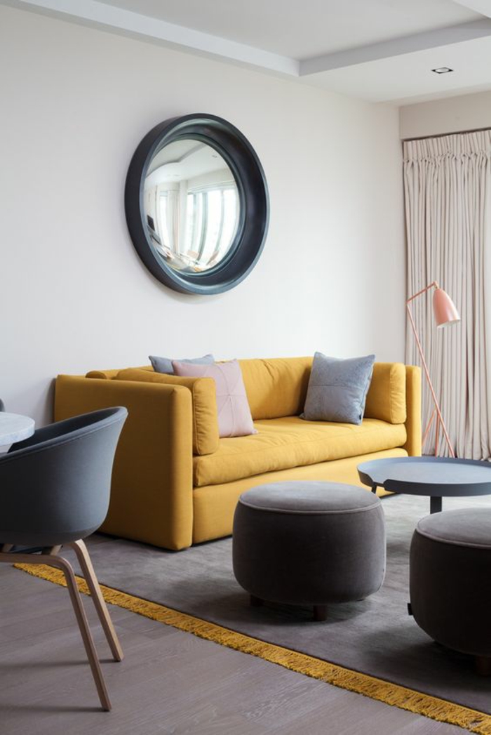 un salon gris et ocre jaune très épuré au mobilier scandinave, un grand miroir convexe original