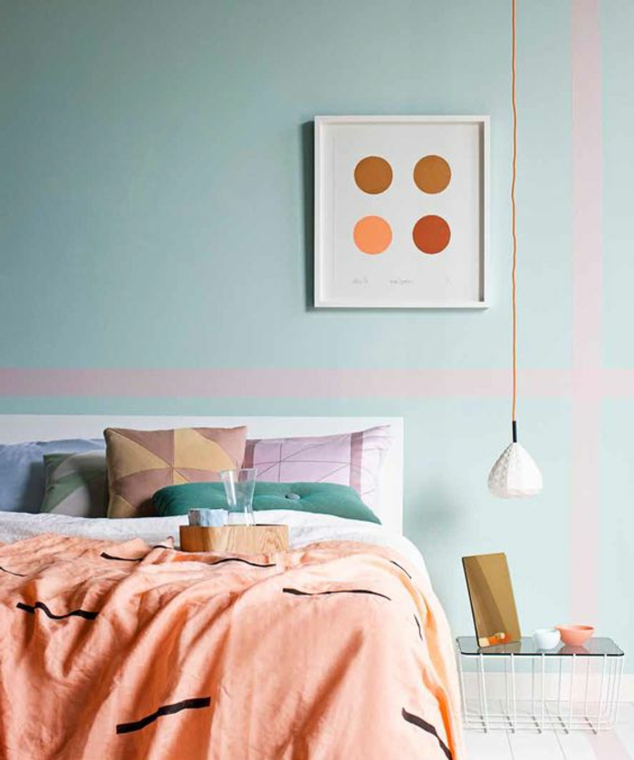 couverture couleur abricot, coussins déco géométriques, lampe blanche pendante, tableau abstrait et mur bleu