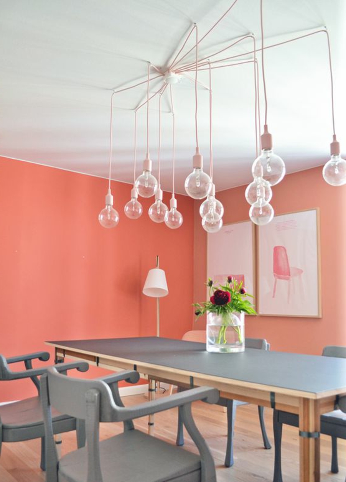 corail couleur, plafond blanc, plusieurs ampoules suspendues, table en bois peinte grise, murs corail
