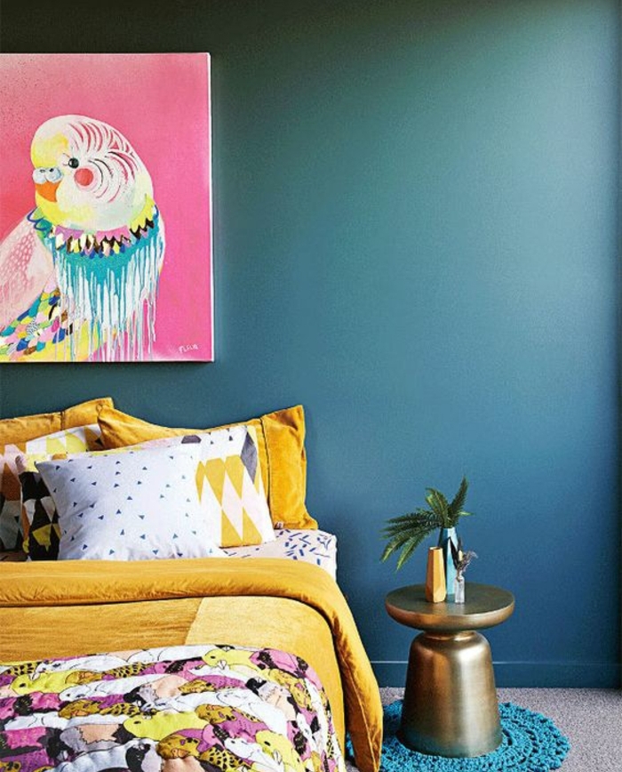 deco bleu canard, couleur mur et linge de lit jaune, couverture multicolore, tableau de peinture, habillage murs, perroquet sur un fond rose, table basse design, coussins multicolores
