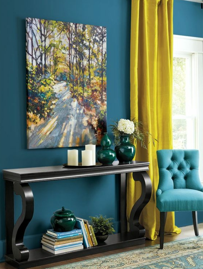 deco bleu canard et jaune, table de service en bois, mur et canapé couleur bleue, tableau peinture paysage foret, bougies vases, livres, tapis oriental, rideau jaune