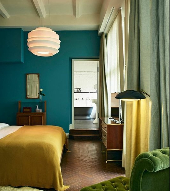 idee deco bleu canard dans une chambre a coucher adulte, fauteuil vert, suspension design blanche, couverture de lit jaune moutarde, parquet en bois, mobilier vintage