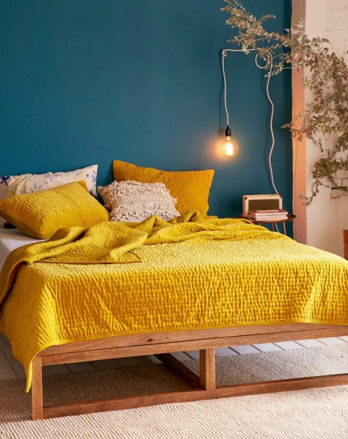 peinture murale deco bleu canard, lit en bois, linge de lit jaune moutarde, tapis beige, ampoule electrique