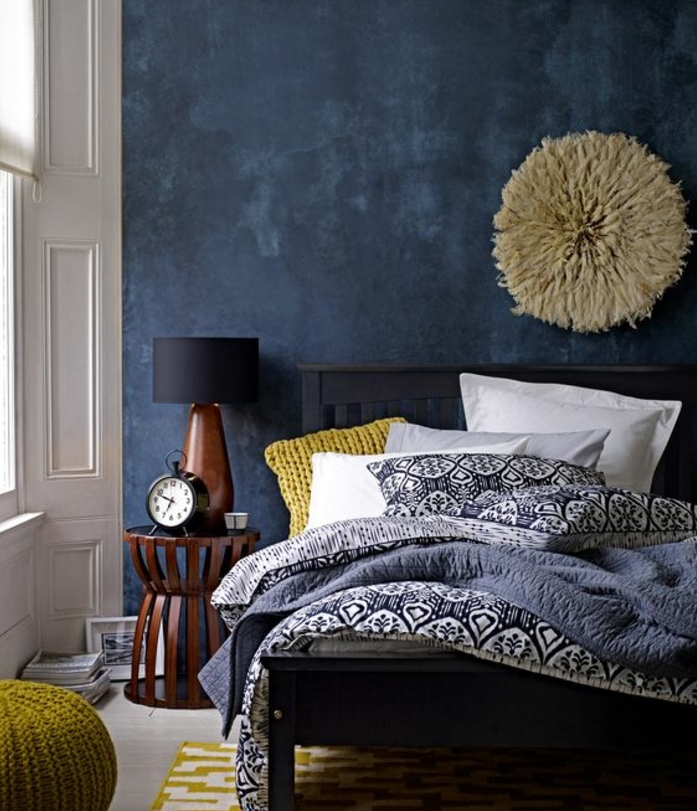 idée déco chambre adulte, lit noire, mur d accent bleu marine, coussin, pouf et tapis jaune, linge de lit motifs orientaux, deco murale intéressante, table de nuit en bois, réveil vintage