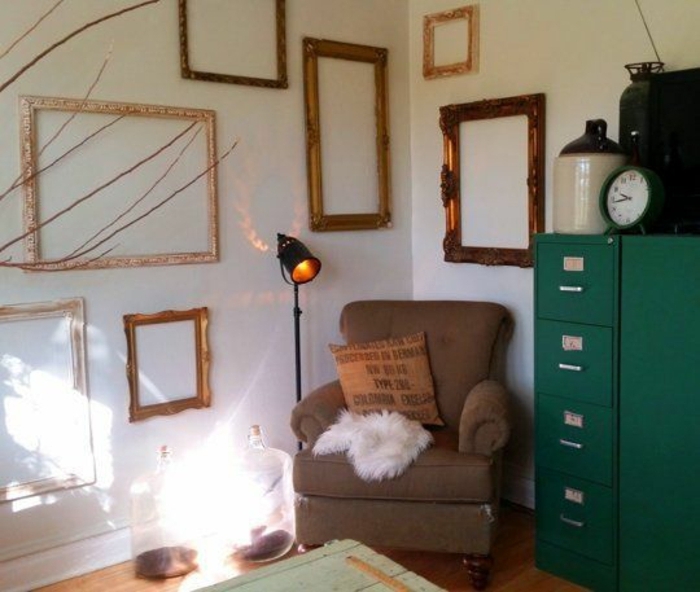 mur de cadres vintage formats divers, meuble de rangement vert, fauteuil marron, mur blanc, table en bois retro, disposition asymétrique