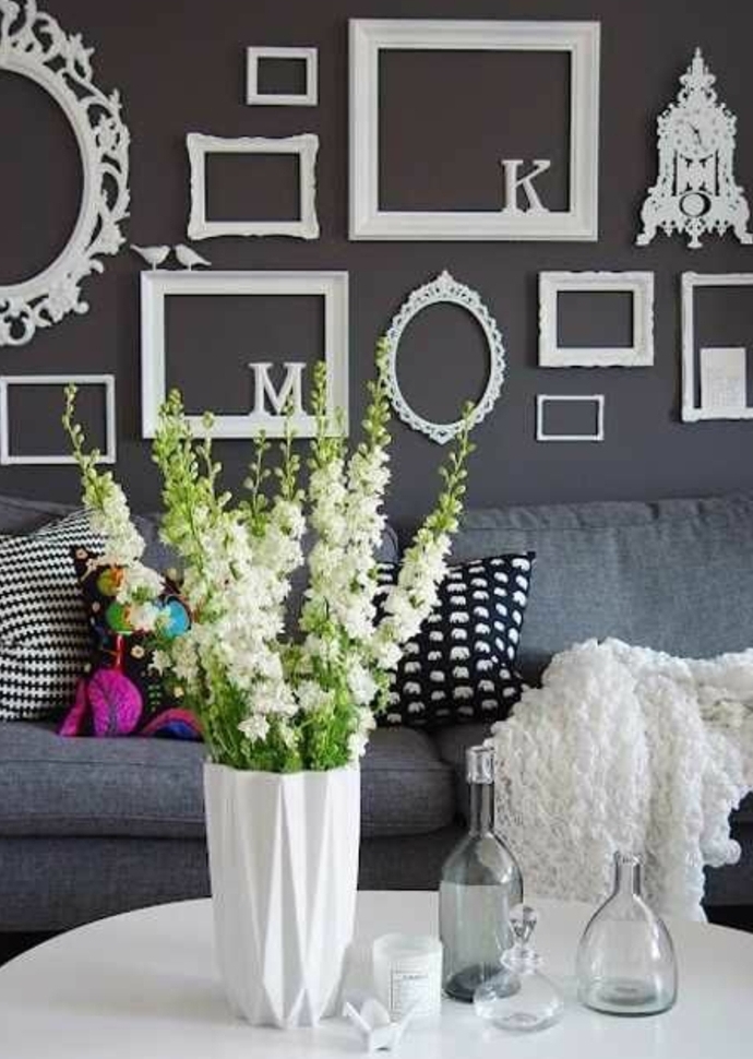 mur de cadres blancs vintage et lettres blanches décoratives, canapé gris, coussins multicolores, vase blanc, table blanche, bouquet de fleurs
