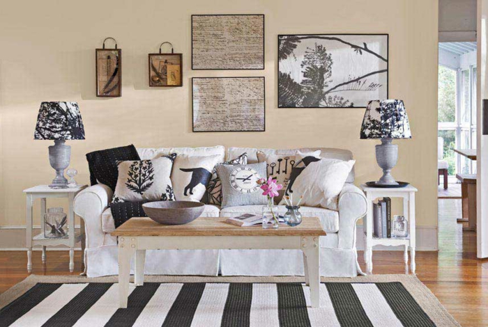 canapé blanc, table basse en bois, tapis à rayures, noir et blanc, coussins en gris, blanc et noir, mur couleur beige, parquet clair, decoration murale
