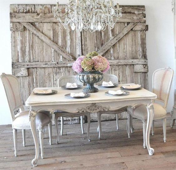 idee deco campagne française, table en bois et chaises blanches, portes en poutres de bois, lustre vintage, centre de table floral