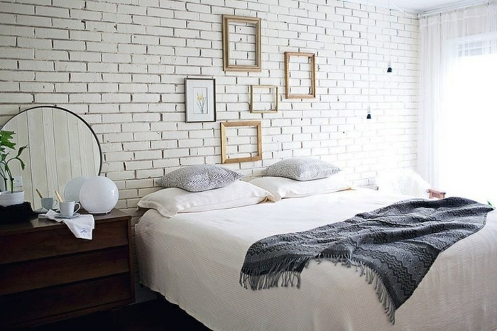 mur de cadres rectangulaires et dessin encadré, mur en briques, table de nuit en bois, linge de lit blanc et gris, decoration de chambre scandinave