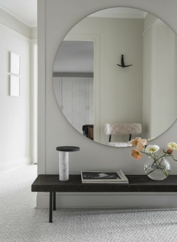 hall d'entrée maison avec grand miroir tout rond et table noire basse sur fond blanc