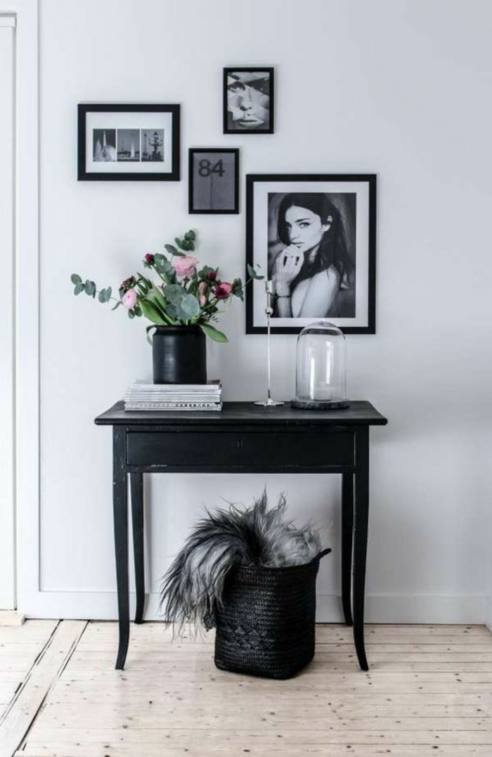 amenagement hall d'entrée maison décoré avec des tableaux aux cadres noirs et table classique noir et panier de rangement en noir