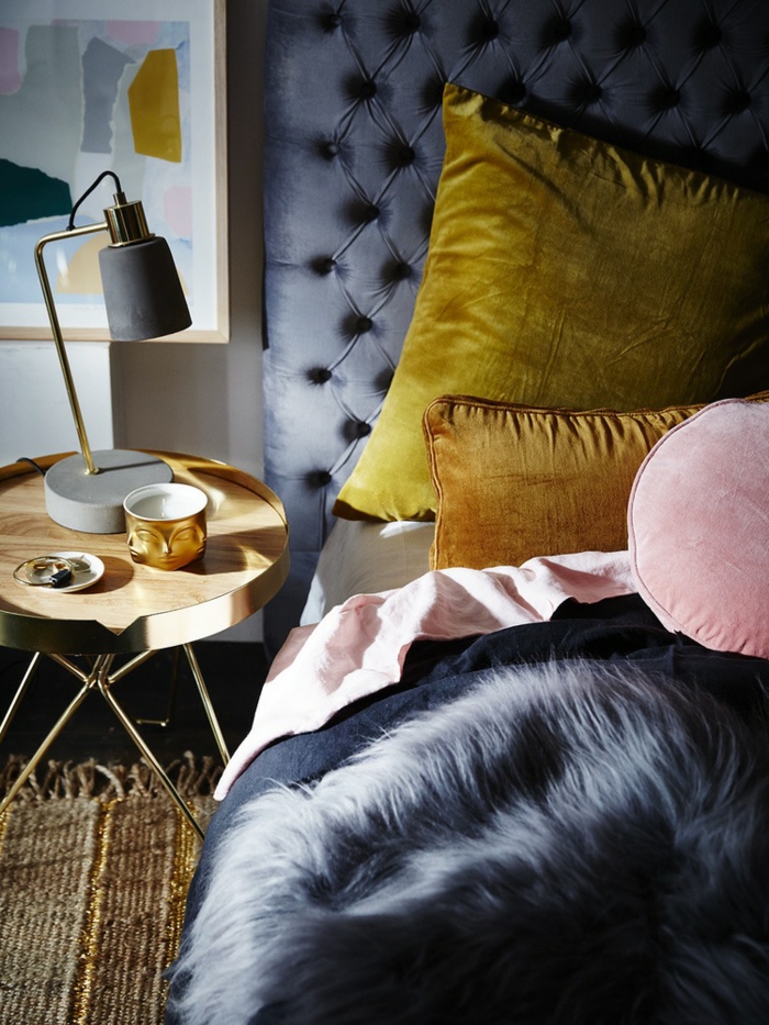 une chambre à coucher élégante aux teintes sombres du bleu dynamisée par des coussins ocre jaune et rose poudré