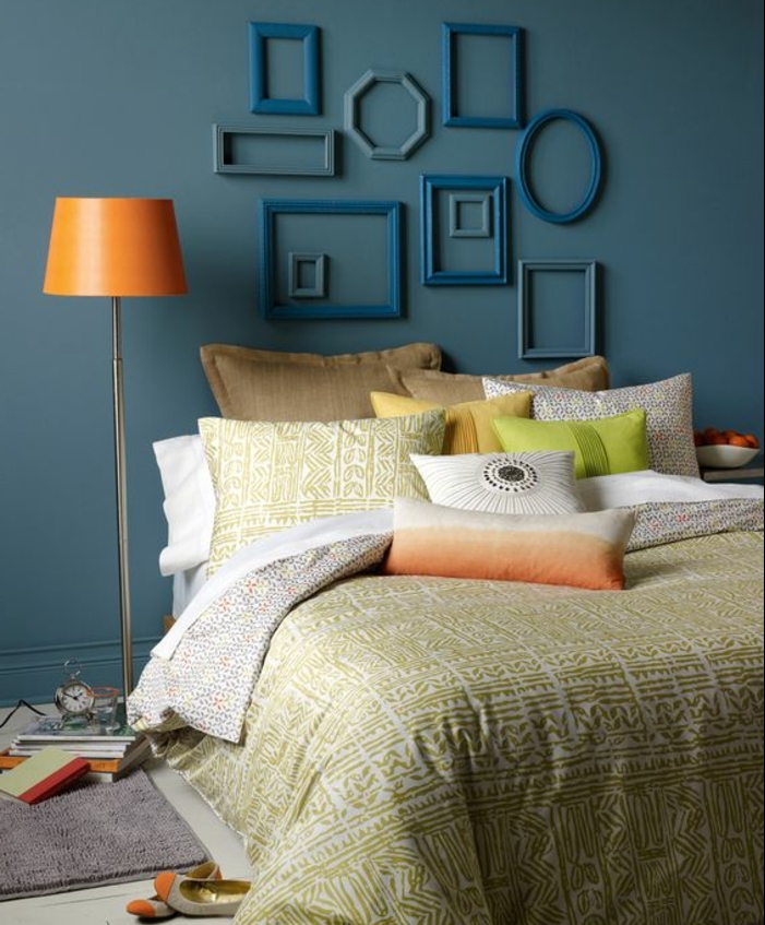 deco chambre a coucher murs couleurs bleu canard, couvertures de lit et coussins en blanc, vert, beige, marron et jaune, deco cadre vide, plusieurs cadres ovales, rectangulaires et carrés, lampe orange