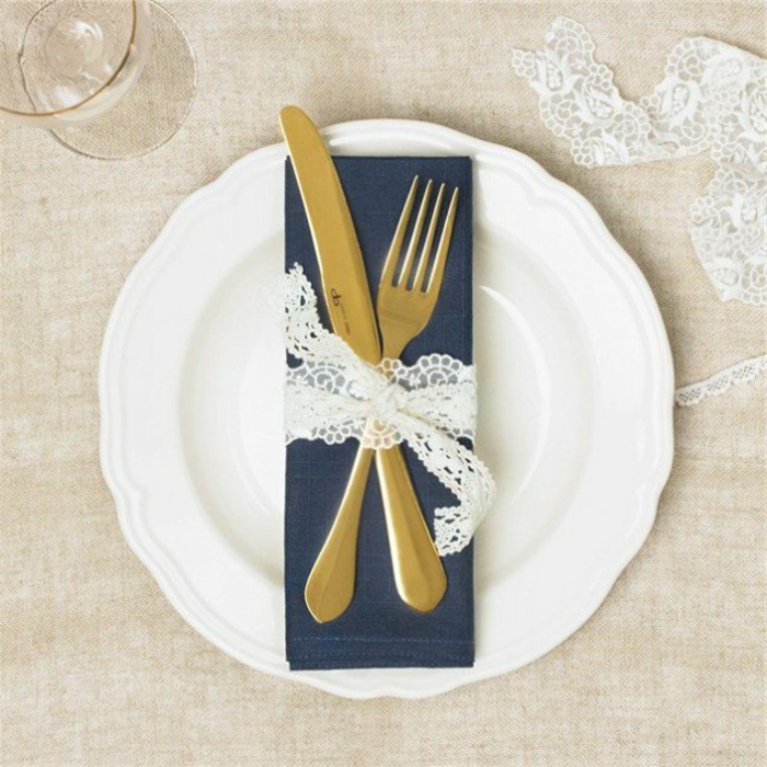 idée décoration mariage, une serviette bleu marin, couverts serrés de bande en dentelle blanche, deco table
