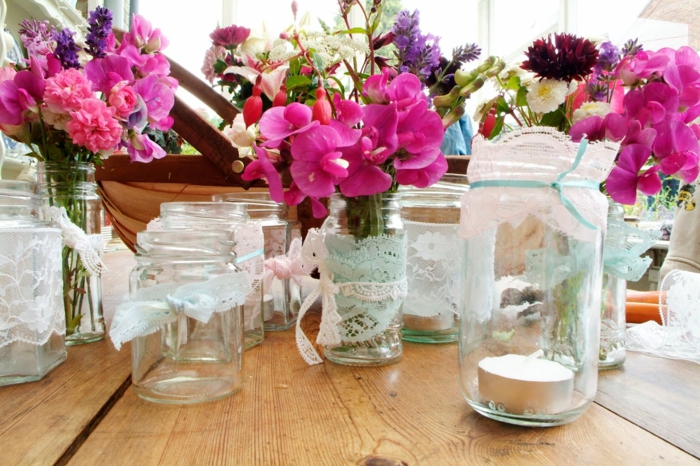 idee deco mariage, des pots en verre customisés de dentelle, bougeoirs et pots de fleurs, remplis de bouquets