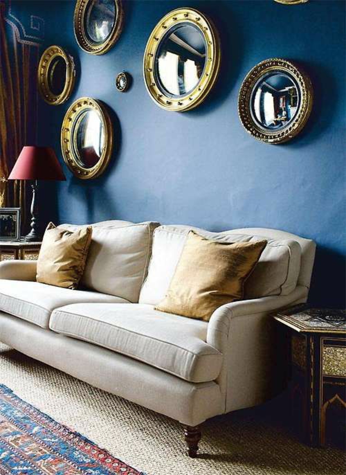 oeil de sorciere miroir 7 pièces sur un mur bleu marin au dessus d'un canapé blanc avec des coussins jaunes 