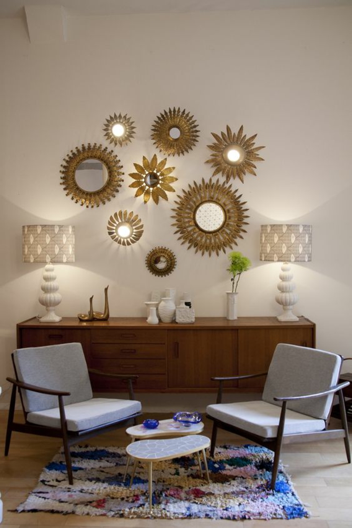 miroir sorcière oeil soleil aux rayons dorés sur un mur blanc composition de miroirs illuminés par deux lampadaires de coté 