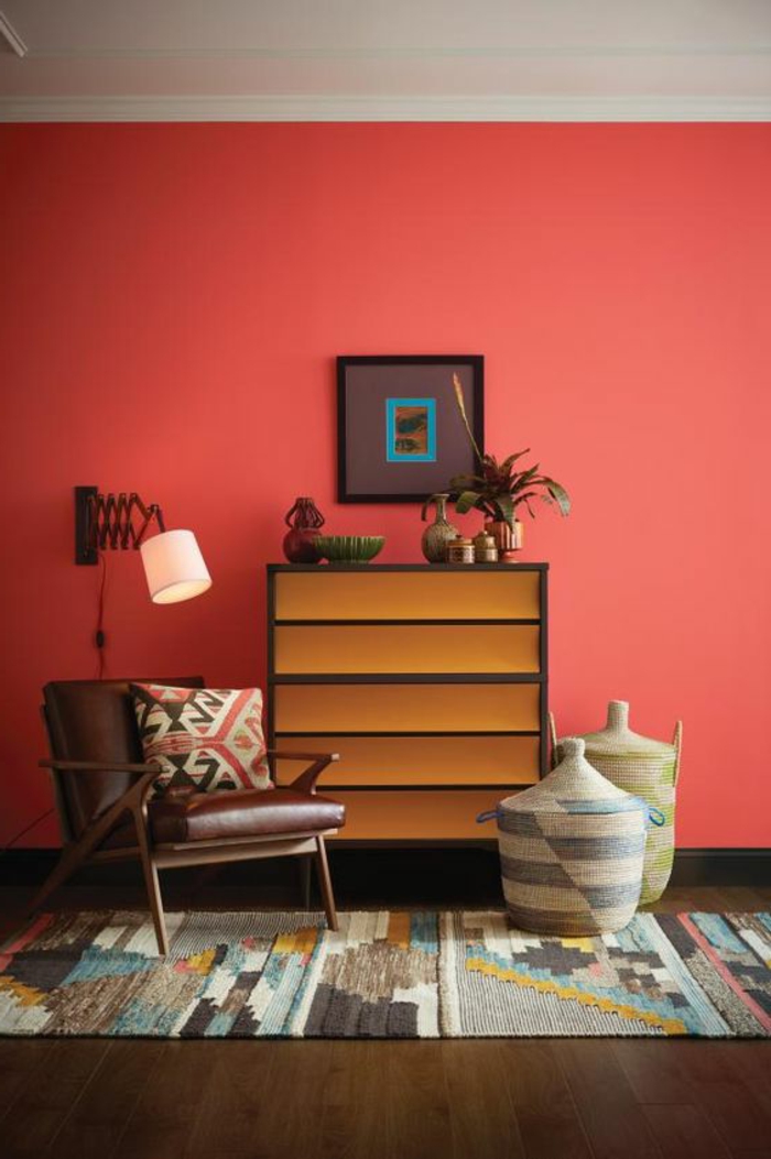 mur couleur rouge corail, carpette bariolée, paniers et chaise en cuir et bois